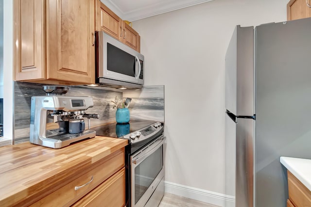 kitchen with crown molding, appliances with stainless steel finishes, butcher block counters, and decorative backsplash