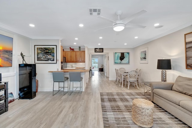 living room featuring ornamental molding, ceiling fan, and light wood-type flooring