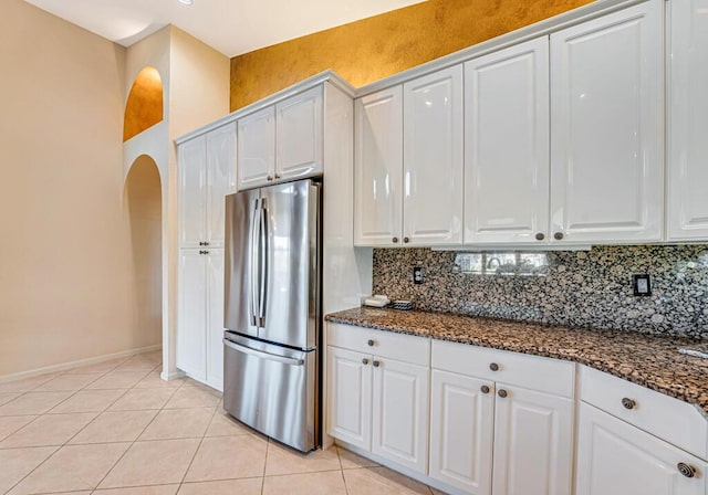 kitchen with light tile patterned flooring, dark stone countertops, white cabinets, stainless steel fridge, and decorative backsplash