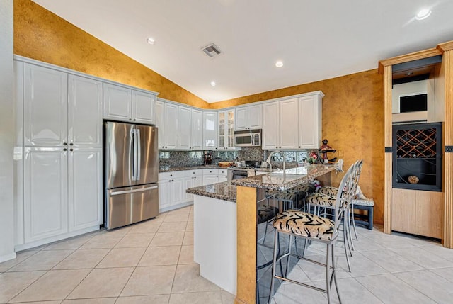 kitchen with appliances with stainless steel finishes, a breakfast bar area, white cabinets, dark stone counters, and kitchen peninsula