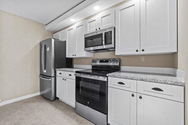 kitchen with appliances with stainless steel finishes, white cabinets, light tile patterned floors, light stone countertops, and a textured ceiling