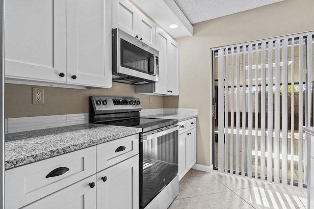 kitchen with appliances with stainless steel finishes, white cabinetry, light tile patterned floors, light stone countertops, and a textured ceiling