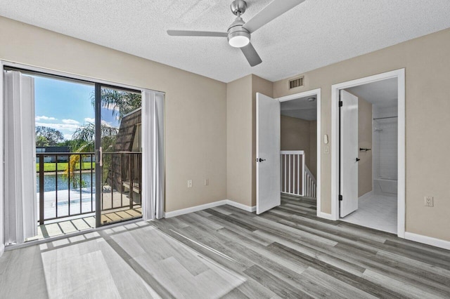 unfurnished bedroom with hardwood / wood-style floors, access to outside, a textured ceiling, and a water view