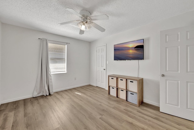 unfurnished living room featuring a textured ceiling, ceiling fan, baseboards, and light wood-style floors