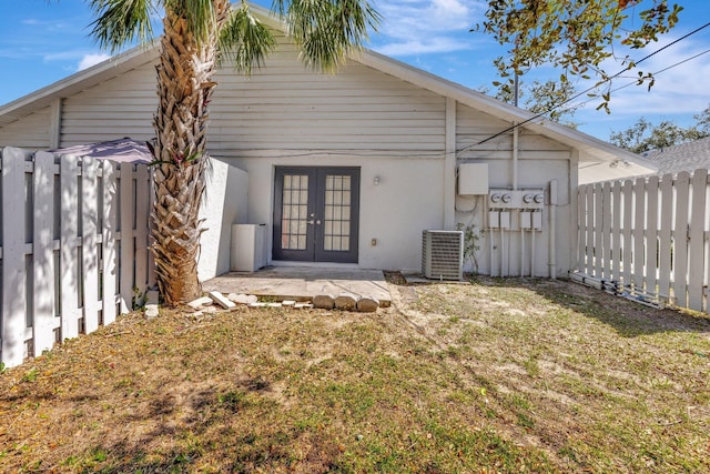 rear view of property with stucco siding, a fenced backyard, central AC, and french doors