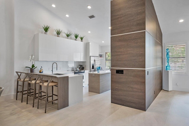 kitchen with appliances with stainless steel finishes, white cabinetry, sink, a kitchen bar, and kitchen peninsula