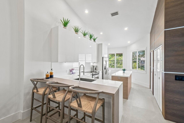 kitchen featuring sink, a breakfast bar area, appliances with stainless steel finishes, white cabinetry, and kitchen peninsula