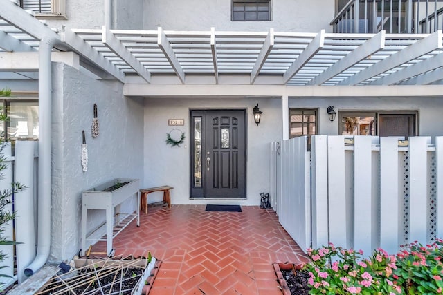 view of exterior entry featuring stucco siding and a pergola