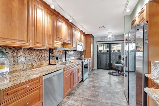 kitchen with backsplash, rail lighting, light stone countertops, and stainless steel appliances