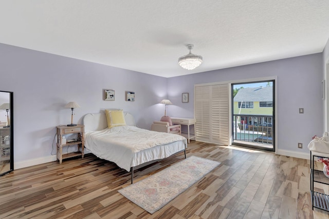 bedroom with a textured ceiling, access to exterior, and hardwood / wood-style flooring