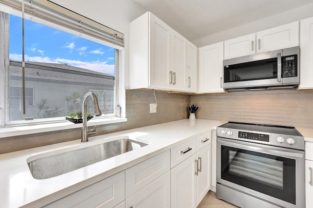 kitchen with sink, tasteful backsplash, appliances with stainless steel finishes, white cabinets, and light tile patterned flooring