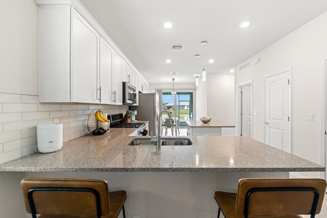 kitchen featuring appliances with stainless steel finishes, sink, white cabinets, a kitchen bar, and kitchen peninsula