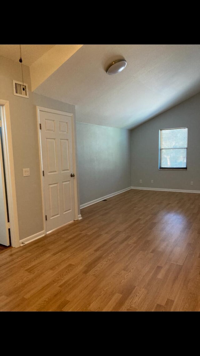 empty room with hardwood / wood-style flooring and vaulted ceiling