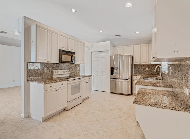 kitchen featuring stone counters, electric stove, a sink, black microwave, and stainless steel fridge