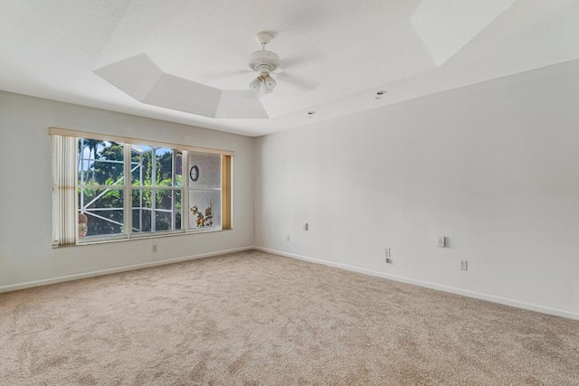 spare room featuring a ceiling fan, a raised ceiling, carpet flooring, and baseboards