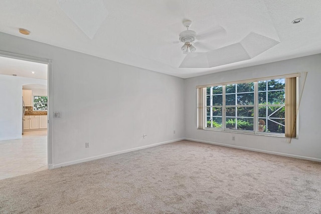 unfurnished room with arched walkways, ceiling fan, carpet floors, baseboards, and a tray ceiling