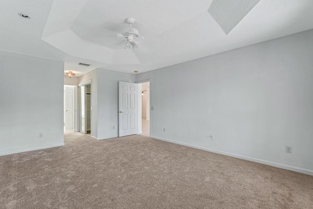 carpeted spare room featuring ceiling fan, a tray ceiling, visible vents, and baseboards