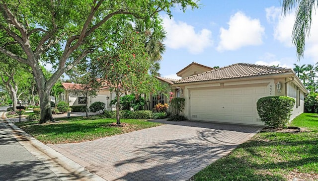 view of front of home with decorative driveway, stucco siding, an attached garage, a tiled roof, and a front lawn