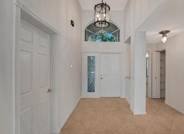 entryway with baseboards, a high ceiling, a chandelier, and light tile patterned flooring