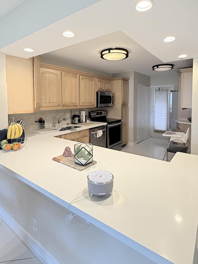 kitchen featuring appliances with stainless steel finishes, sink, decorative backsplash, kitchen peninsula, and light brown cabinets