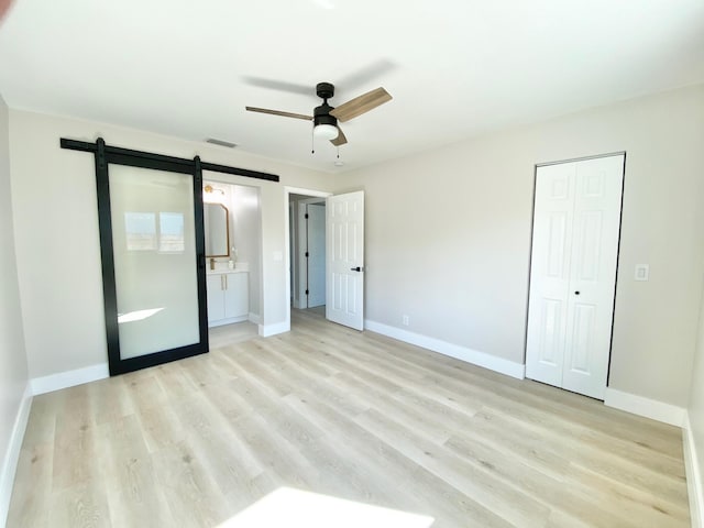 unfurnished bedroom with ceiling fan, ensuite bathroom, a barn door, a closet, and light wood-type flooring