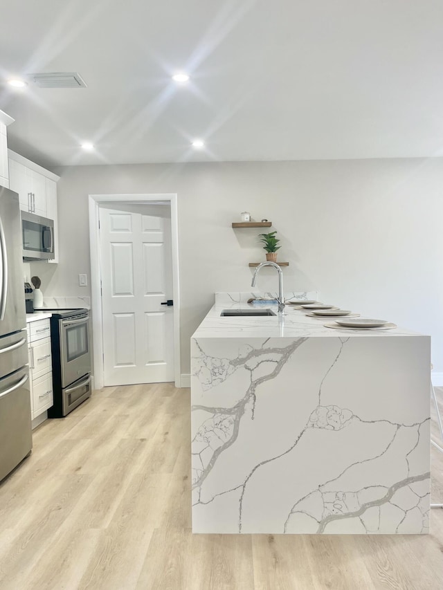 kitchen featuring sink, white cabinetry, stainless steel appliances, light hardwood / wood-style floors, and light stone countertops