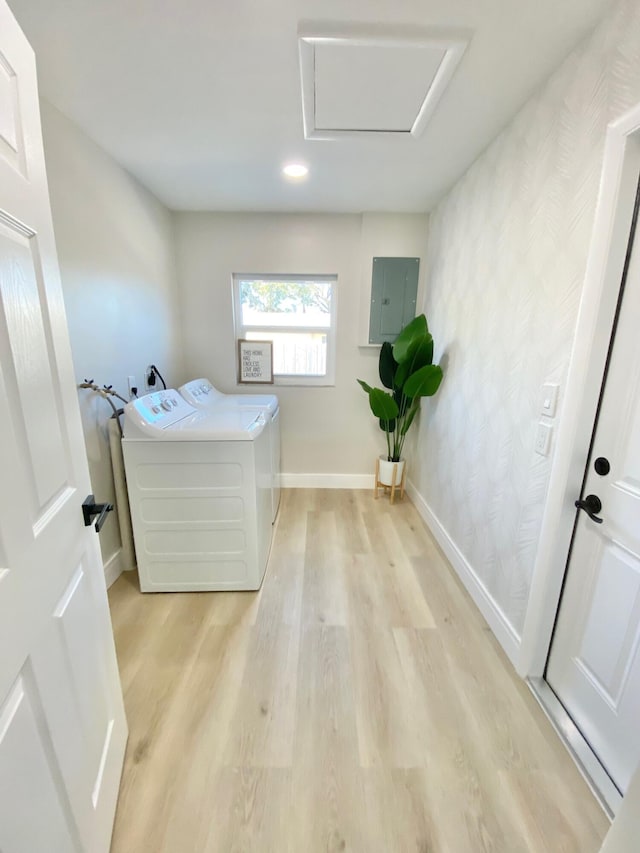 laundry room featuring electric panel, washing machine and dryer, and light hardwood / wood-style flooring