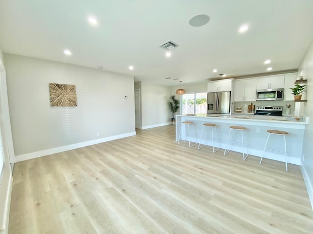 kitchen with a breakfast bar area, white cabinets, kitchen peninsula, stainless steel appliances, and light wood-type flooring