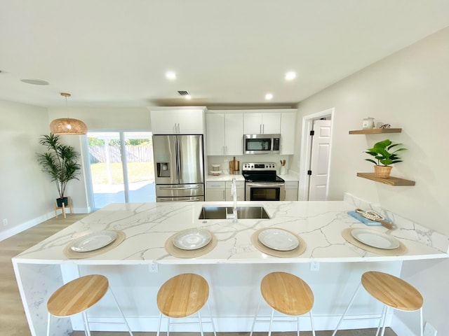 kitchen with white cabinetry, appliances with stainless steel finishes, light stone counters, and decorative light fixtures