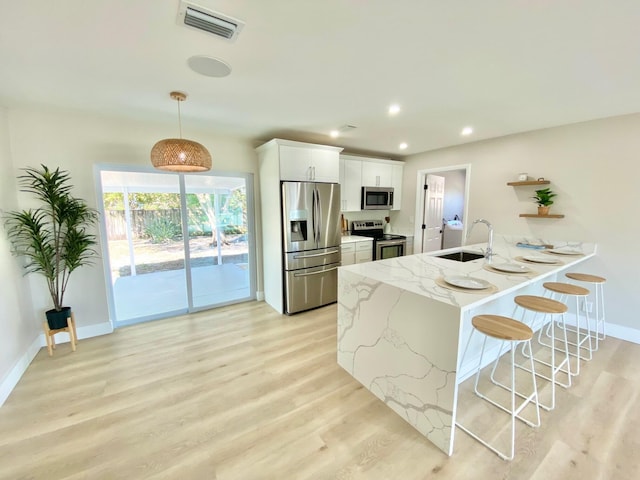 kitchen with sink, hanging light fixtures, stainless steel appliances, light stone counters, and white cabinets