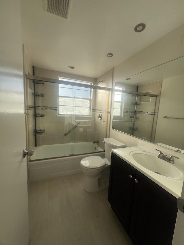 full bathroom with vanity, hardwood / wood-style floors, bath / shower combo with glass door, and toilet