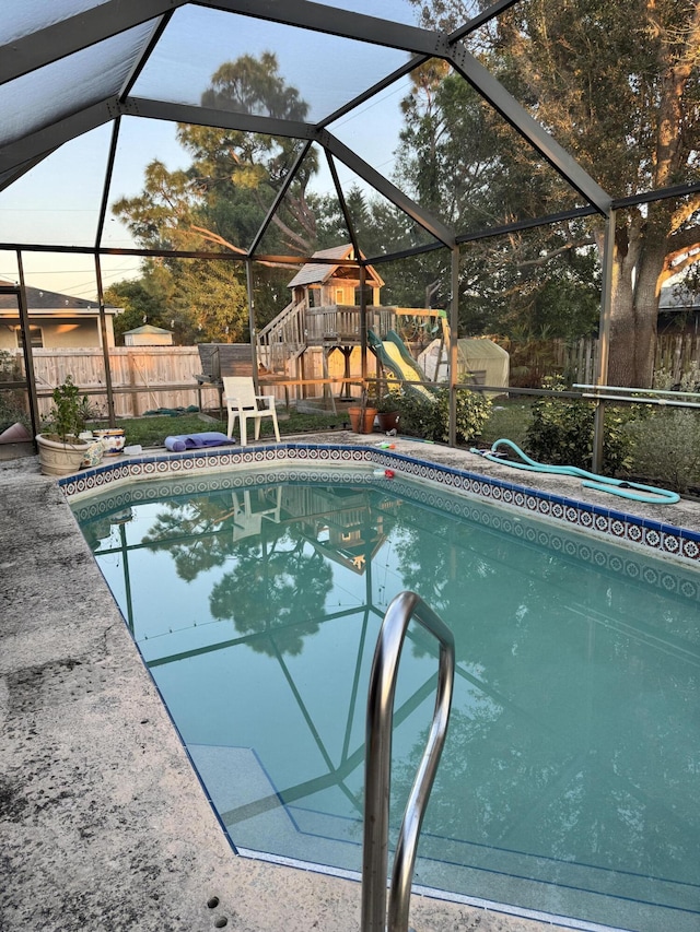 pool at dusk featuring a playground and a lanai