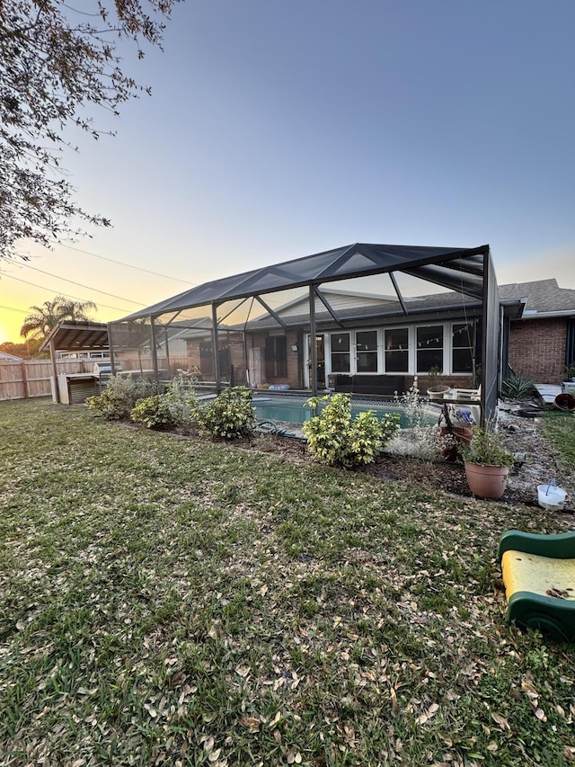 back house at dusk featuring a yard and glass enclosure