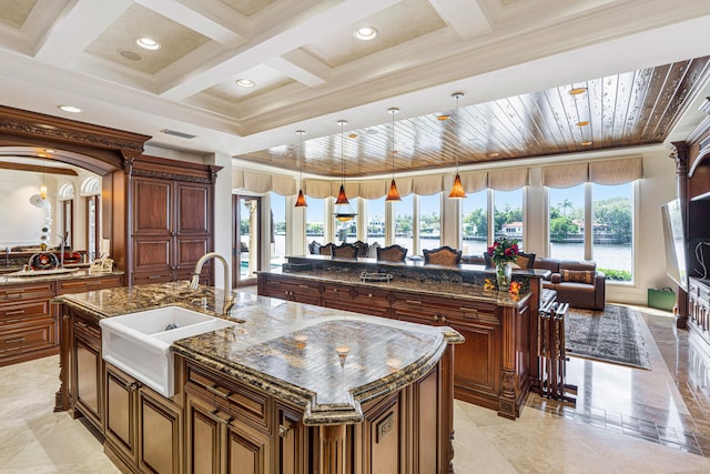 kitchen featuring sink, decorative light fixtures, an island with sink, and dark stone counters