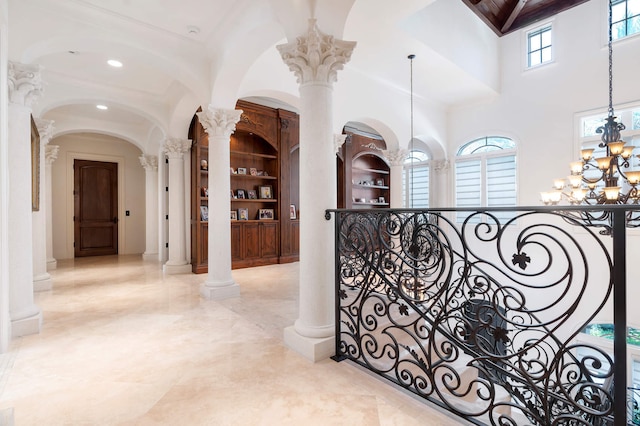 hallway with an inviting chandelier, a towering ceiling, built in shelves, and decorative columns