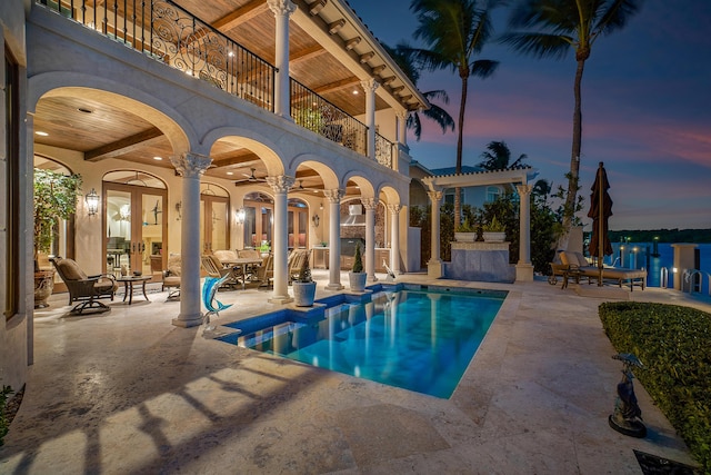 pool at dusk featuring a patio, ceiling fan, a pergola, a water view, and french doors