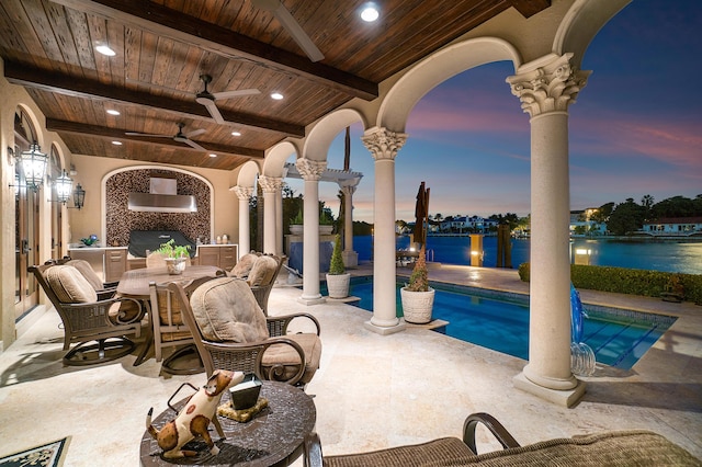 patio terrace at dusk featuring a grill, ceiling fan, and a water view