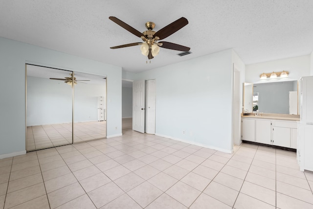 unfurnished bedroom with connected bathroom, a textured ceiling, light tile patterned floors, a closet, and ceiling fan