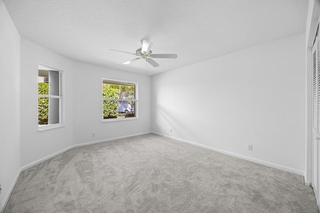 empty room with ceiling fan, light colored carpet, and a textured ceiling