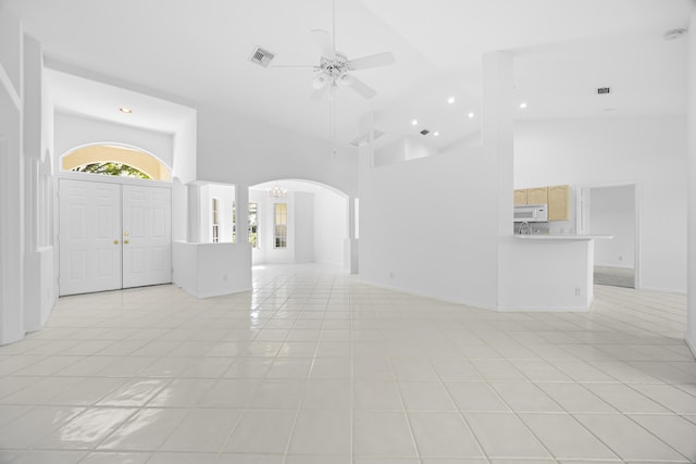 unfurnished living room featuring ceiling fan with notable chandelier, high vaulted ceiling, and light tile patterned floors