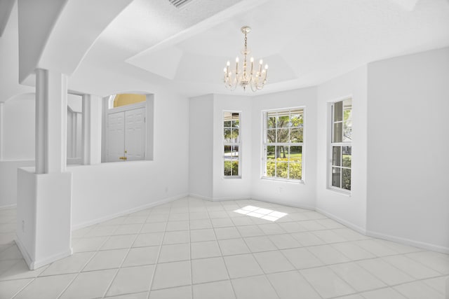 tiled spare room featuring a notable chandelier and a tray ceiling