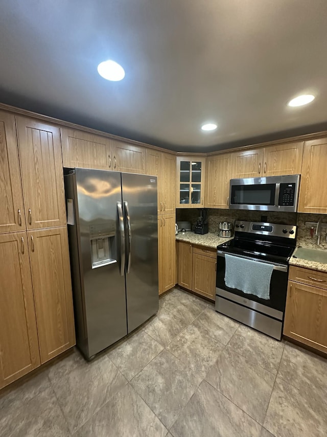 kitchen with stainless steel appliances, light stone countertops, and backsplash