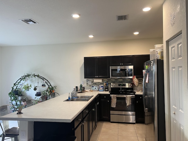 kitchen featuring appliances with stainless steel finishes, sink, decorative backsplash, light tile patterned floors, and kitchen peninsula