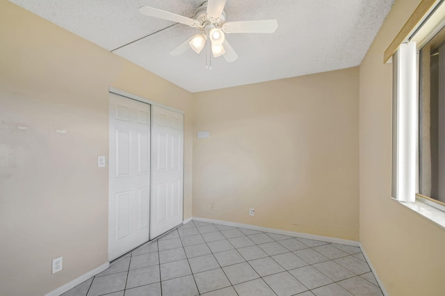 unfurnished bedroom with light tile patterned flooring, a textured ceiling, ceiling fan, and a closet