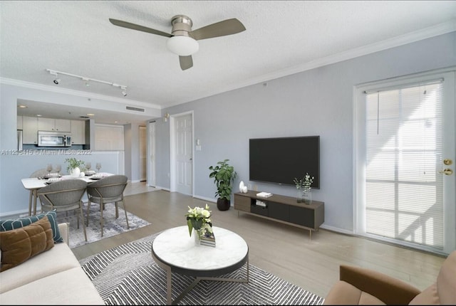 living room with rail lighting, a textured ceiling, ornamental molding, ceiling fan, and light hardwood / wood-style floors