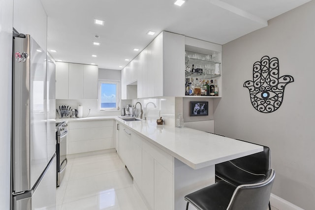 kitchen with a peninsula, light countertops, stainless steel appliances, a sink, and light tile patterned flooring