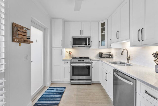 kitchen with tasteful backsplash, sink, white cabinets, stainless steel appliances, and light stone countertops