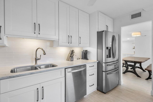 kitchen with sink, white cabinetry, stainless steel appliances, tasteful backsplash, and light stone countertops