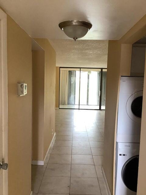 hall with light tile patterned flooring and stacked washer and clothes dryer