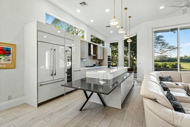 kitchen with gas cooktop, hanging light fixtures, a center island, paneled refrigerator, and light wood-type flooring